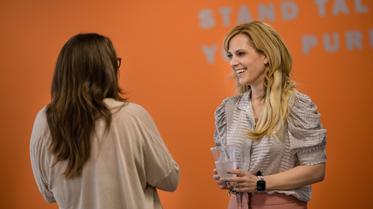 two women talking in front of orange wall