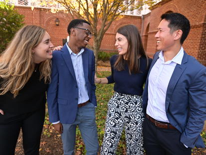 Four students stand in the foreground, laughing and smiling