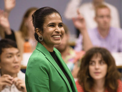 Professor in green coat teaching AI to a classroom of students.