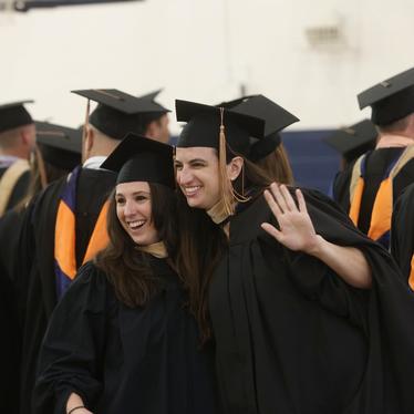 two women in graduation caps and gowns smile and wave